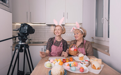 two elderly women in rabbit ears on their heads shoot a video blog looking into the camera. Preparations for the Easter holiday