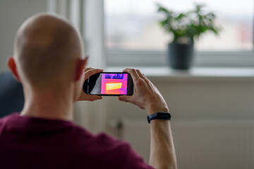 Person doing thermal scanning or imaging of apartment with smartphone app. Thermographic Inspection to check effectiveness of insulation