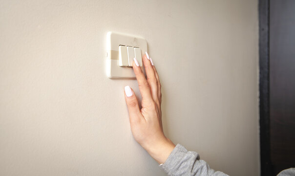 Female hand turning an electricity light switch on the wall.