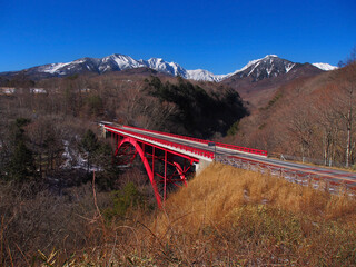 冠雪した山と谷に架かる赤い橋(八ヶ岳と東沢のアーチ橋)
