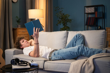 A young boy with dark curly hair lies on a couch in the living room in homespun clothes leaning...
