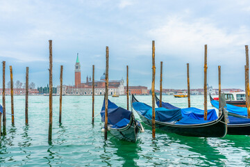 December 2, 2021 - Venice, Italy: Gondolas moored at Sam Marco Gondola Service Station on Grand Canal with Chiesa di San Giorgio Maggiore on the background.