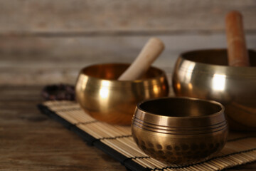 Golden singing bowls and mallets on wooden table, space for text