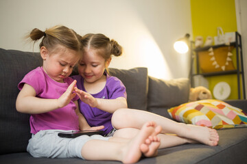 sister's children are sitting at home on couch, looking at phone, communicating via video and waving. kids gadget apps