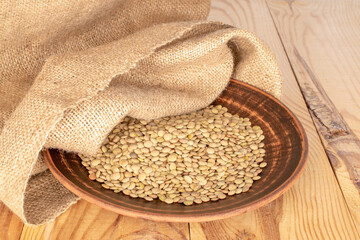 Dry organic green lentils with clay dish and burlap sack on wooden table.