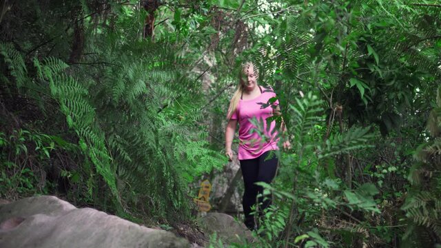 Front view of female hiker in pink shirt walking confident in tropical forest.
