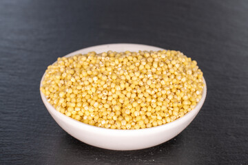 Dry organic millet in a white saucer on a slate stone.