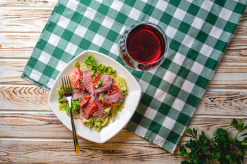 Healthy green salad with meat, tomato and lettuce served in a square white plate with a glass of red wine.