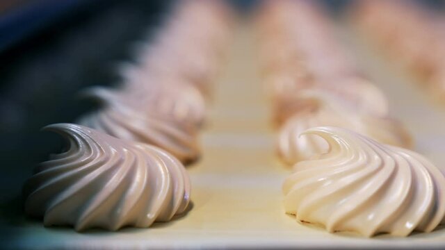 Manufacturing white zephyr candies at modern confectionery factory. Creamy sweets moving along the conveyor. Close up. Blurred backdrop.
