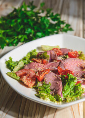 Healthy green salad with meat, tomato and lettuce served in a square white plate over grey or gray background.