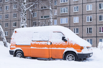 Orange car, van covered snow after snowfall and blizzard on town street in courtyard of apartment...