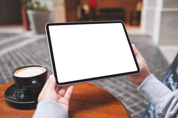 Mockup image of a woman holding digital tablet with blank white desktop screen with coffee cups on the table