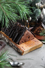 Chocolate cake with chocolate cream and glaze decorations on a wooden board. Sweet treats on a table with pine branches