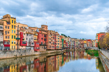 Obraz premium Landscape of Girona with Gomez or Princess Bridge over the river Onyar, Spain. Town panorama with bright multi-colored old houses and their reflections in the water stream