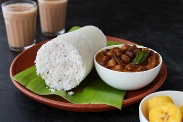 Popular South Indian breakfast puttu / pittu made of rice flour and coconut with banana and kadala curry, Kerala breakfast, India. Bamboo puttu prepared in steam 