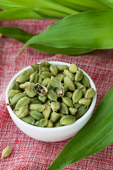 Heap of fresh organic green cardamom pods spice Indian spices for Indian cooking Masala hot spicy curry whole spices wooden spoon leaves Kerala India Sri Lanka.