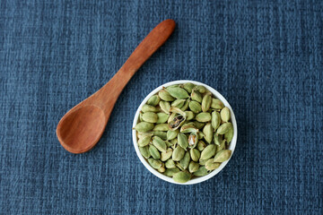 Heap of fresh organic green cardamom pods spice Indian spices for Indian cooking Masala hot spicy curry whole spices wooden spoon leaves Kerala India Sri Lanka.