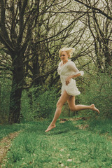A beautiful young woman in a white chiffon dress with a short blonde haircut runs along the path...