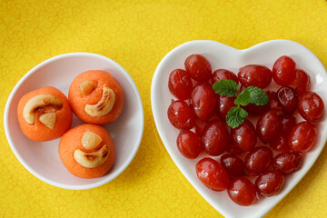 Organic fresh sweet red cherry and Indian mithai  rava laddu besan ladoo in white heart shaped plate for Valentines Day couples a romantic treat dessert. love 