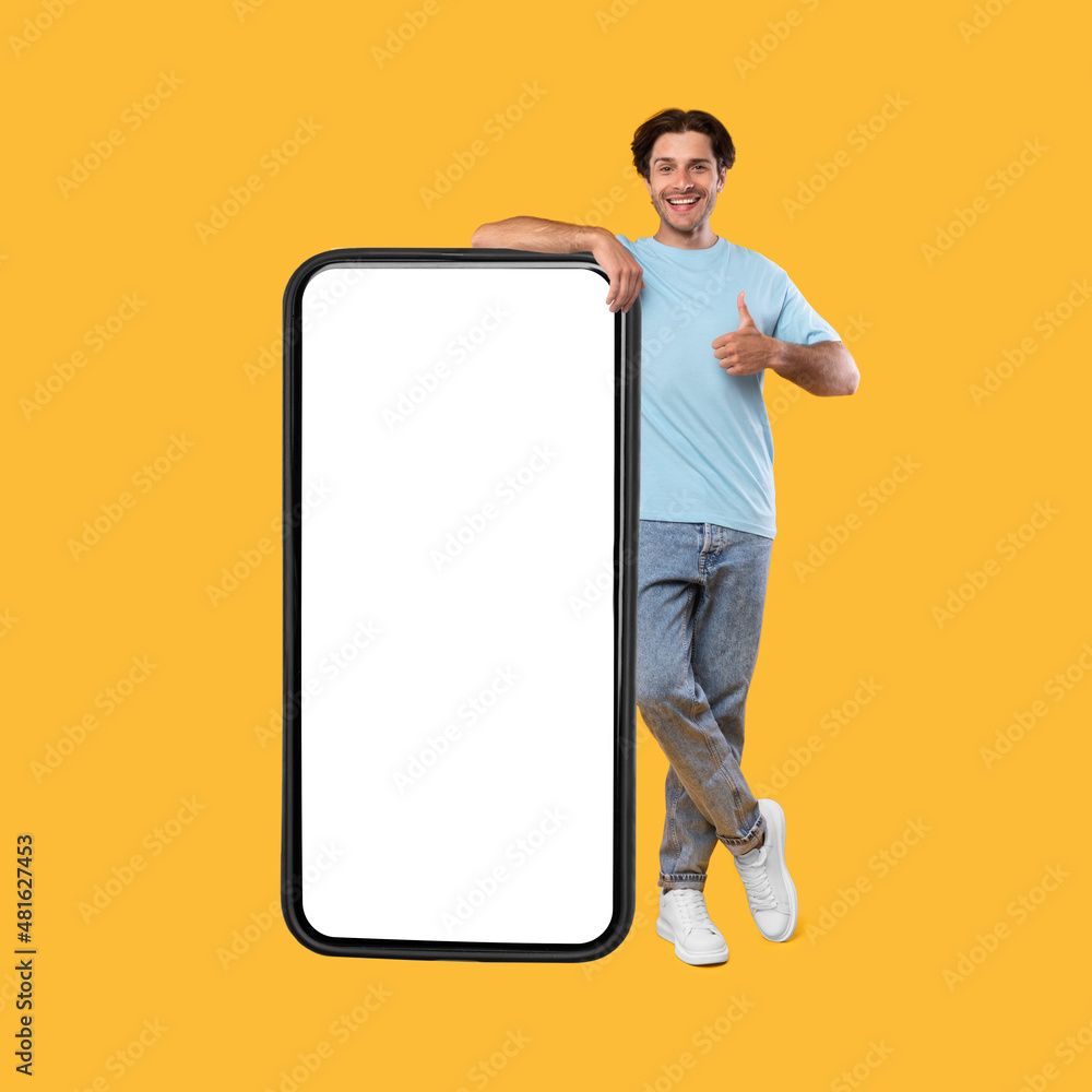 Wall mural Happy man showing white empty smartphone screen and thumbs up