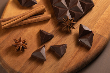 Dark bitter chocolate is broken into pieces. Decorated with cinnamon sticks. Brown background. Flatlay