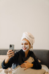 Young woman with face mask using mobile phone while sitting in bed