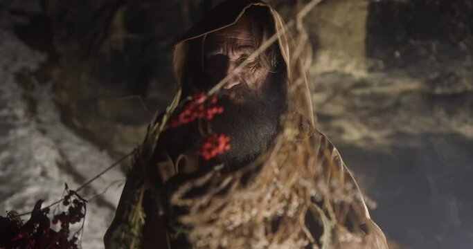Old magician chooses ingredients for potion in dark cave