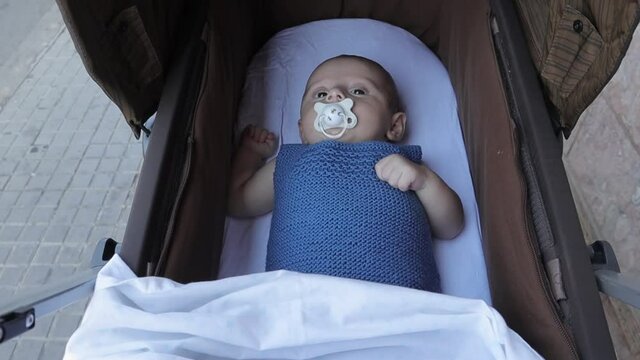 Little baby sucking a pacifier while enjoying a ride in the stroller.