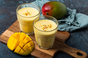 Healthy Indian Ayurveda drink mango lassi in two glasses on rustic concrete table with fresh ripe...
