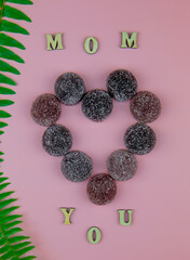 Stylish text frame with the inscription mom love you from fruity natural diet marmalade. Top view of wooden letters on a pink background.