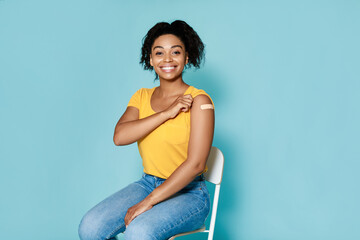 Young black woman with plaster band aid after covid vaccine shot smiling on blue studio background