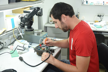 a young man in the workshop repairs an electrical appliance at his desk sitting in an armchair
