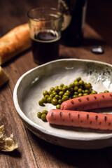 Grilled sausages with green peas served with dark beer and artisan bread on wooden table. Bachelor's dinner. Selective focus