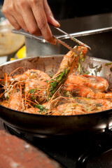 Chef preparing prawn in a pan on a stove in a kitchen.