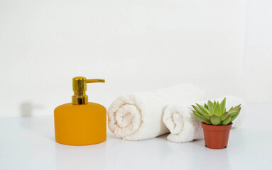 Fototapeta na wymiar Clean white bath towels, a place to copy. Towel, yellow soap dispenser, flower, accessories on a white background background. Elegant bathroom interior decor.