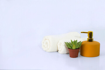 Clean white bath towels, a place to copy. Towel, yellow soap dispenser, flower, accessories on a white background background. Elegant bathroom interior decor.