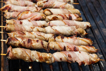 Meat wrapped in bacon on wooden skewers is grilled.