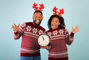Five minutes to New Year. Overjoyed black couple with clock showing five minutes till midnight,...