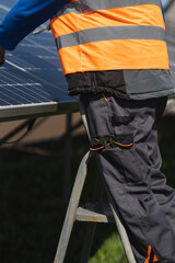Fototapeta na wymiar Male engineer who installs and maintains solar panels stands on a stepladder and takes out a wrench from his pocket