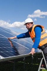 Solar power plant worker on stepladder makes a visual inspection of solar panels