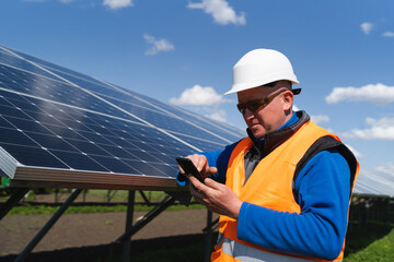 Man in hard hat using smartphone on the background of solar panels