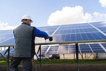 Back view of a man works with a drill screwdriver on solar panels