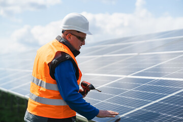 Male worker in uniform with a drill - screwdriver in his hand on a stepladder near solar panels