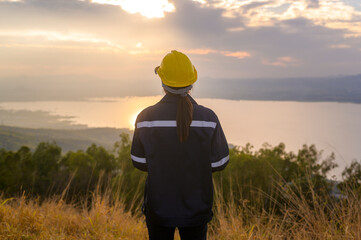 a woman engineer is putting a protective helmet on her head at sunset.