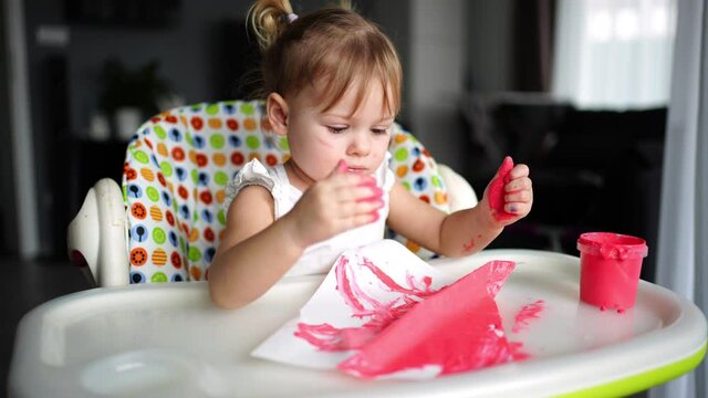 Cute little girl painting with fingers at home. Creative games for kids. Stay at home entertainment