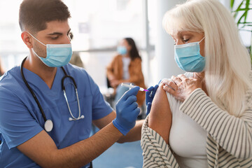 Mature Woman Receiving Vaccine Injection Sitting With Doctor Indoor