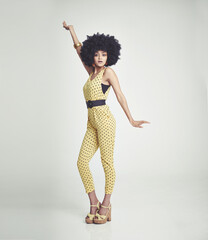 Feeling the 70s vibe. A young woman wearing a 70s retro jumpsuit and striking a disco pose while in the studio. © Yuri Arcurs/peopleimages.com