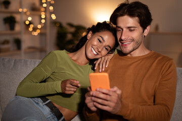 Happy Couple Using Smartphone Sitting On Sofa At Home