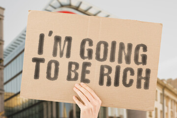 The phrase " I'm going to be rich " on a banner in men's hand with blurred background. Prosperous. Destination. Risk. Strategy. Profit. Profitable. Employment. Productive