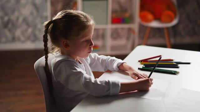 Girl draws illustration on paper sitting in children room